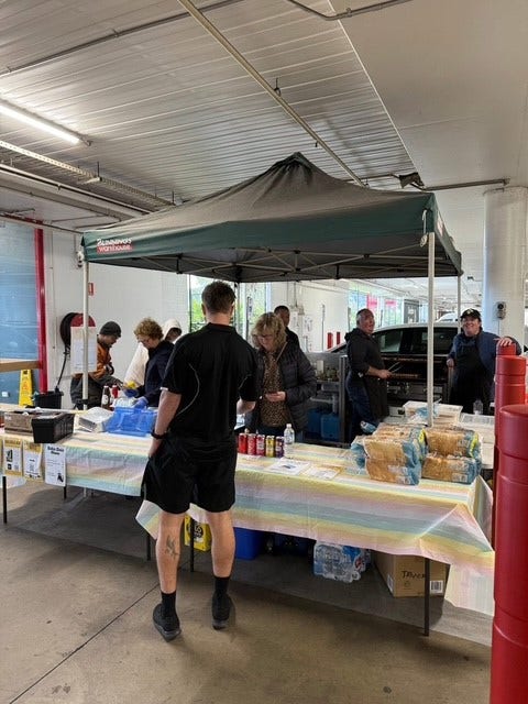 A table with people serving sausage sandwiches at bunnings.